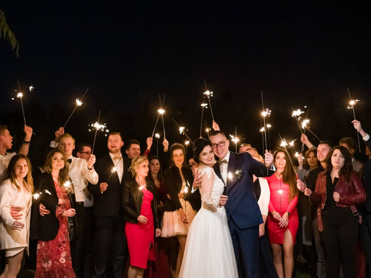 Para Młoda z gośćmi trzymają zapalone zimne ognie